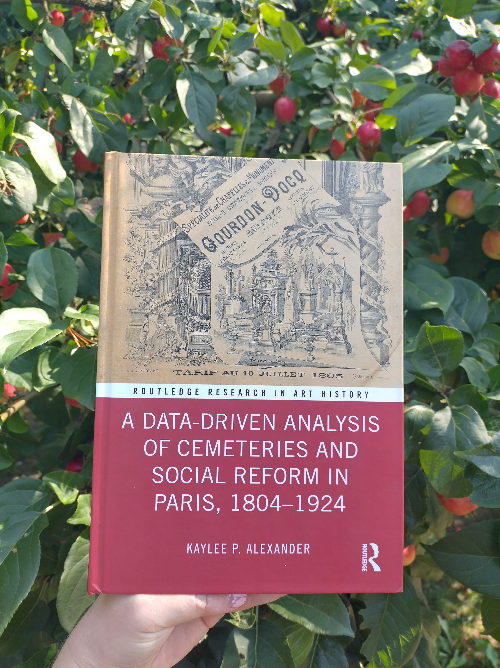 Photo of a data driven analysis of cemeteries and social reform in Paris in front of an apple tree with red apples. Picture taken for dead good reading